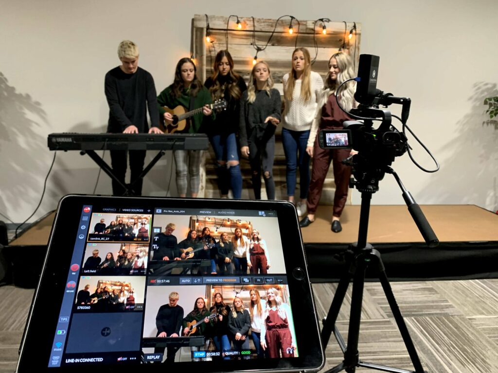 A group of five young women and a young man playing music while being filmed.