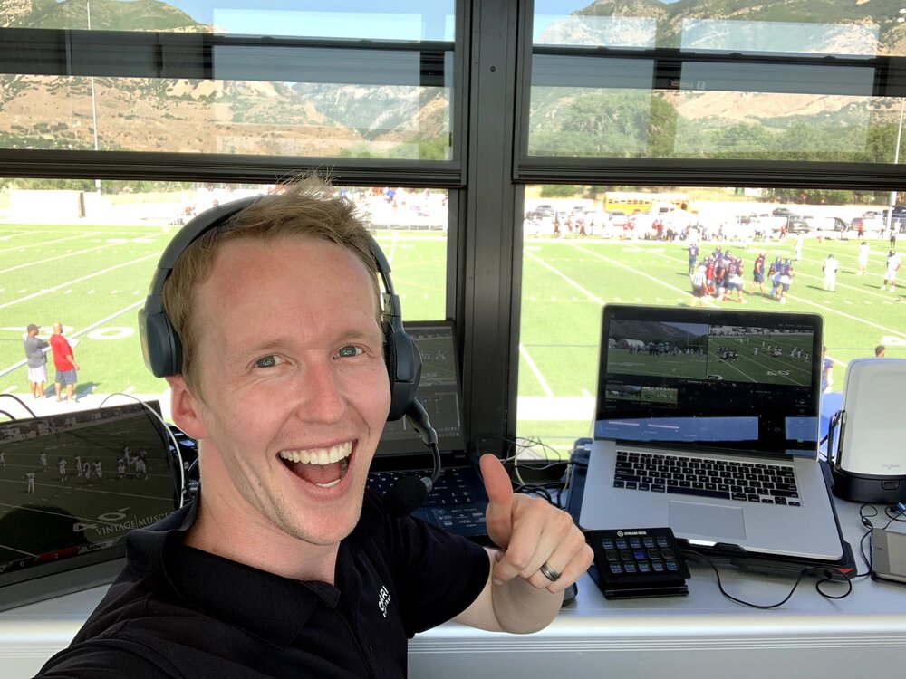 Cooper Brown giving a thumbs up and a smile in the broadcasting booth of a semi-pro football game.