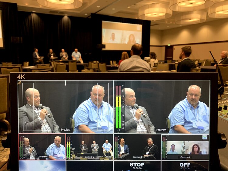 A monitor with several frames of two men speaking at a conference.