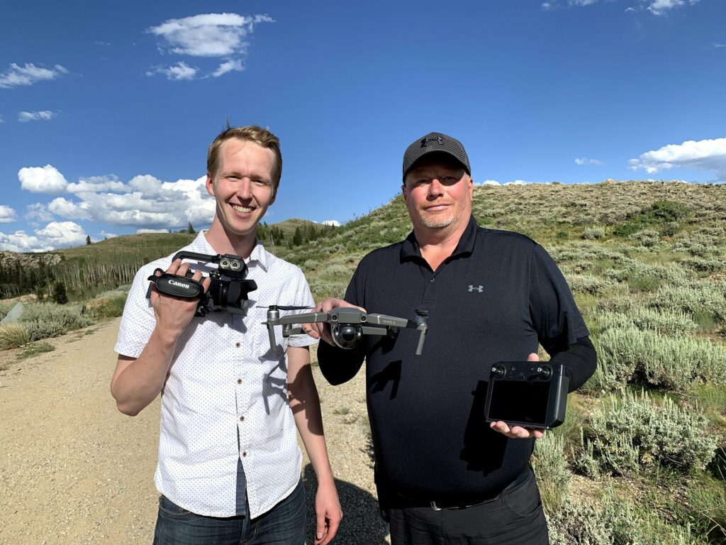 Two men with a drone and a videocamera in a western landscape on a beautiful day.