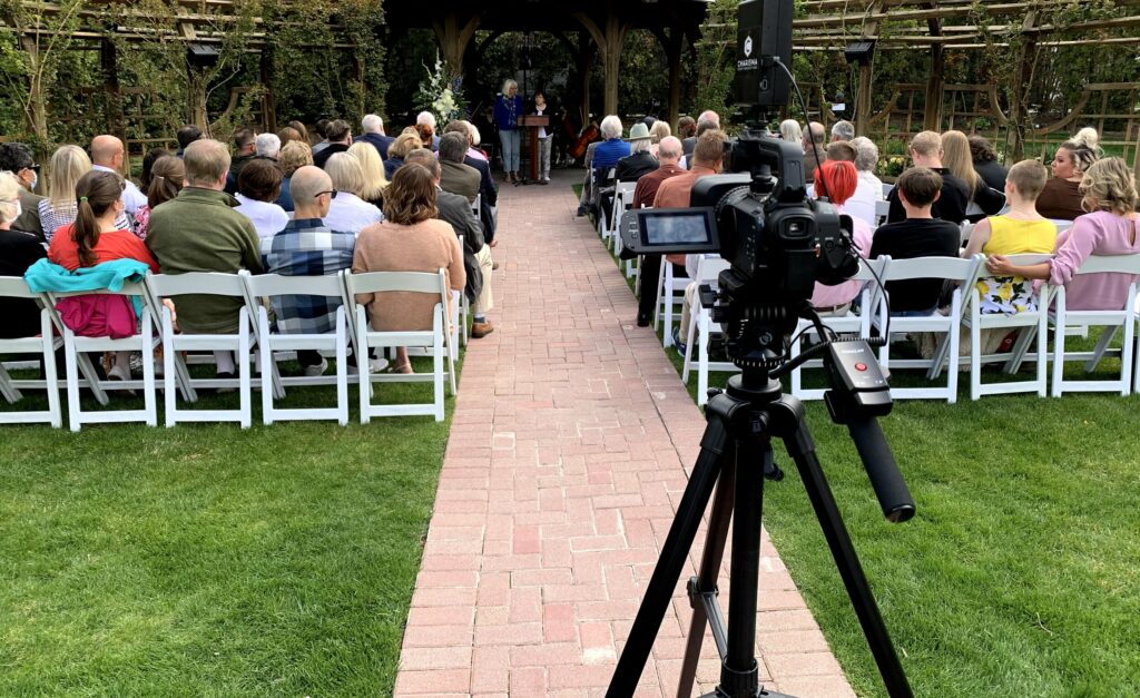 A videocamera filming an outdoor funeral ceremony.