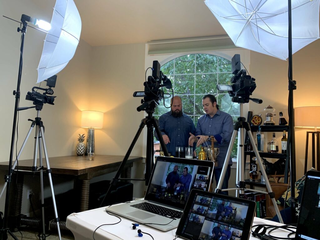 Two men being filmed as they prepare cocktails at a table.